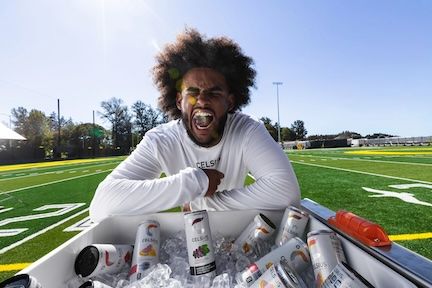 Man in a Celsius shirt shouting over a cooler full of Celsius cans on a football field