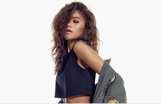 Zendaya posing in a black top and olive jacket